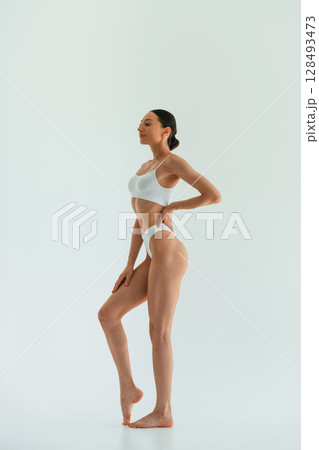 In white fitness clothes. Young woman with slim body type is in the studio 128493473