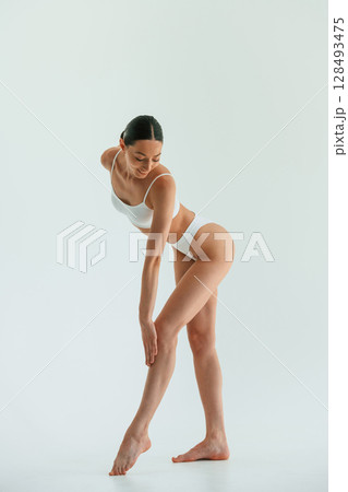 In white fitness clothes. Young woman with slim body type is in the studio 128493475