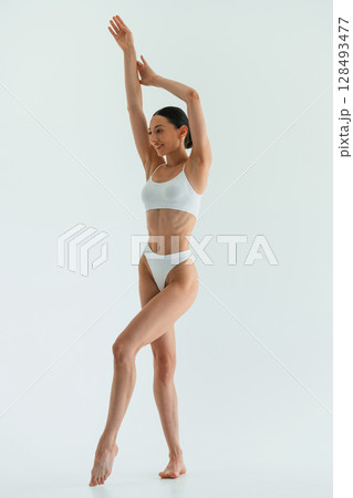 With hands up. Young woman with slim body type is in fitness clothes in the studio 128493477