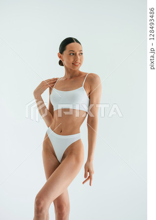 Feeling good. Standing and smiling. Young woman with slim body type is in fitness clothes in the studio 128493486