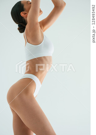 Raising hands up. Young woman with slim body type is in fitness clothes in the studio Raising hands up. Young woman with slim body type is in fitness clothes in the studio 128493492