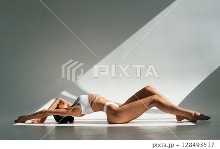 Straightens the back up, sitting on the floor. Young woman with slim body type is in fitness clothes in the studio 128493517