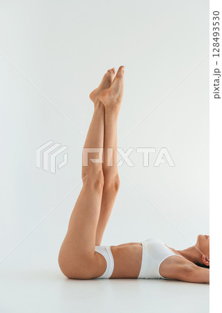 Legs are up, lying down. Young woman with slim body type is in fitness clothes in the studio 128493530