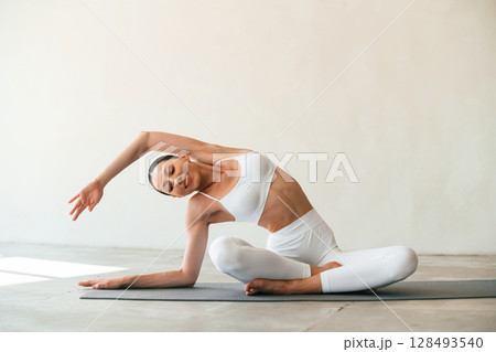 Using yoga mat for exercises. Young woman with slim body type is in fitness clothes in the studio 128493540