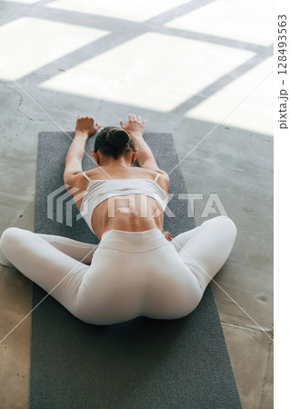 Using yoga mat for exercises. Young woman with slim body type is in fitness clothes in the studio 128493563