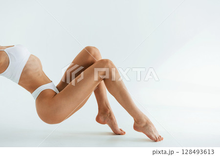 View from the side, on the floor. Young woman with slim body type is in fitness clothes in the studio 128493613