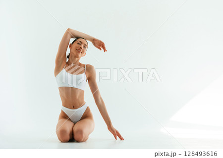 Front view, on the floor. Young woman with slim body type is in fitness clothes in the studio 128493616