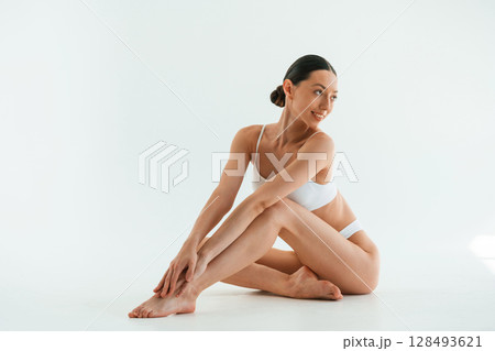 Sitting on the floor. Young woman with slim body type is in fitness clothes in the studio Sitting on the floor. Young woman with slim body type is in fitness clothes in the studio 128493621