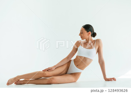 Taking a break, sitting on the floor. Young woman with slim body type is in fitness clothes in the studio Taking a break, sitting on the floor. Young woman with slim body type is in fitness clothes in the studio 128493626