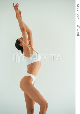 Raising hands up. Young woman with slim body type is in fitness clothes in the studio Raising hands up. Young woman with slim body type is in fitness clothes in the studio 128493639