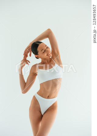 Hands behind the neck and up. Young woman with slim body type is in fitness clothes in the studio Hands behind the neck and up. Young woman with slim body type is in fitness clothes in the studio 128493657