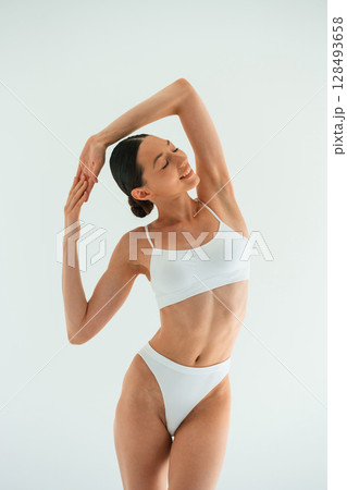 Relaxed, standing against white background. Young woman with slim body type is in fitness clothes in the studio Relaxed, standing against white background. Young woman with slim body type is in fitness clothes in the studio 128493658