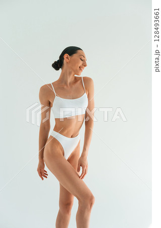 Relaxed, standing against white background. Young woman with slim body type is in fitness clothes in the studio Relaxed, standing against white background. Young woman with slim body type is in fitness clothes in the studio 128493661