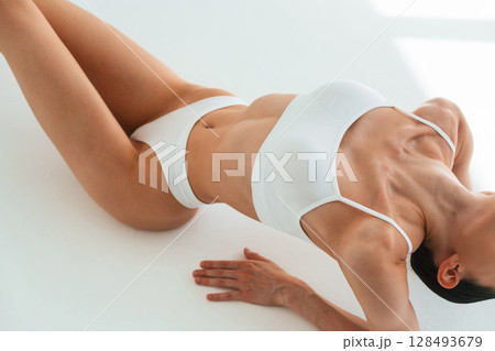 Straightens the back up, sitting on the floor. Young woman with slim body type is in fitness clothes in the studio 128493679