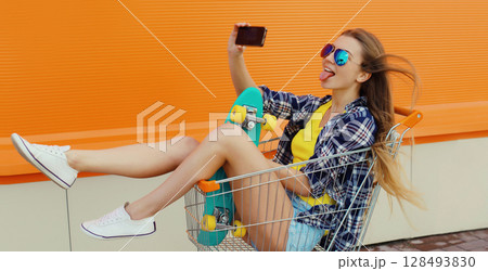 Stylish young woman taking selfie with phone, cool teenage girl in shopping trolley cart in the city 128493830