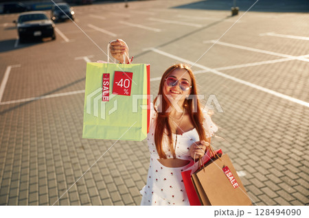 Crazy sales sticker. Beautiful woman in casual clothes is holding shopping bags, outdoors Crazy sales sticker. Beautiful woman in casual clothes is holding shopping bags, outdoors 128494090