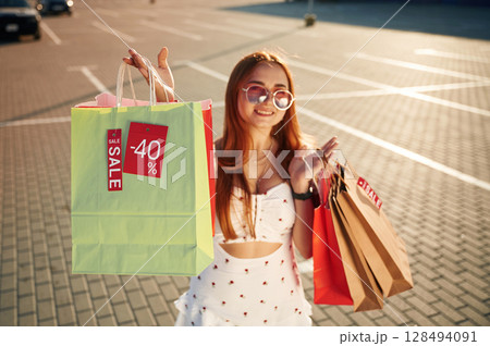 Crazy sales sticker. Beautiful woman in casual clothes is holding shopping bags, outdoors 128494091