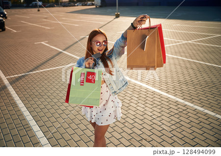 Hurry up for the sale. Beautiful woman in casual clothes is holding shopping bags, outdoors 128494099
