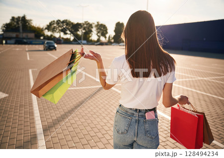Rear view. Beautiful woman in casual clothes is holding shopping bags, outdoors Rear view. Beautiful woman in casual clothes is holding shopping bags, outdoors 128494234