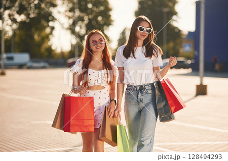 Two beautiful women in casual clothes are holding shopping bags, outdoors Two beautiful women in casual clothes are holding shopping bags, outdoors 128494293
