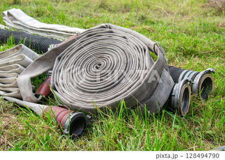 Fire hose rolled up on lawn, lying on grass 128494790