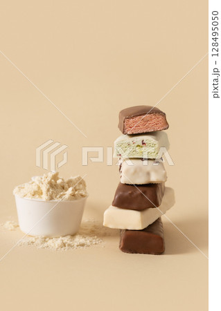Different whey protein bars with various coatings and sprinkles scoop of protein powder on beige background. Fitness nutrition. Vertical format. 128495050