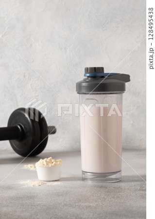 Whey protein shake and dumbbell on gray background. Close up. 128495438