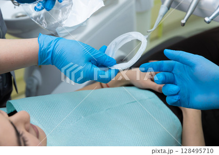 Dental Procedure in Action: Dentist Preparing Tools and Patient for Treatment with Protective Gear and Essential Dental Equipment Dental Procedure in Action: Dentist Preparing Tools and Patient for Treatment with Protective Gear and Essential Dental Equipment 128495710