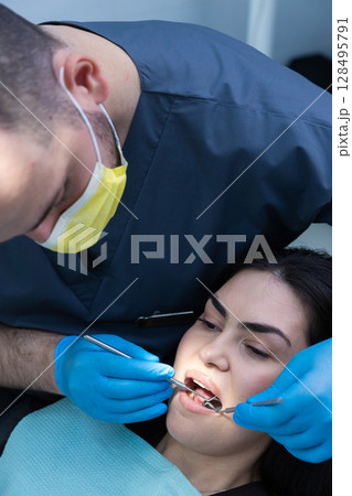 A Dental Professional Providing Care: A Close-Up on an Oral Examination with Patient Receiving Dental Treatment with Proper Protective Gear and Equipment for Safety A Dental Professional Providing Care: A Close-Up on an Oral Examination with Patient Receiving Dental Treatment with Proper Protective Gear and Equipment for Safety 128495791