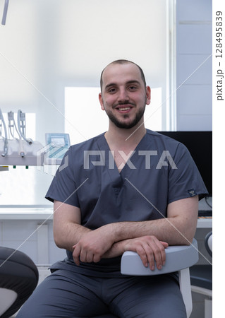 Friendly Dentist Sitting in a Modern Dental Clinic Ready to Provide Excellent Care with a Smile to His Patients in a Bright and Inviting Environment 128495839