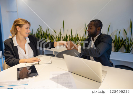 Two colleagues sitting at desk smiling while planning project using laptop tablet and notebook 128496233
