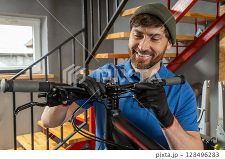 Mechanic repairing bicycle gears in workshop with window on background Mechanic repairing bicycle gears in workshop with window on background 128496283