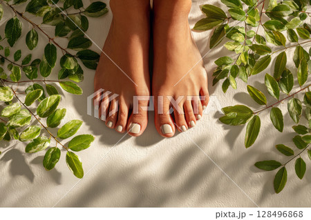 Female feet on light background with green leaves 128496868