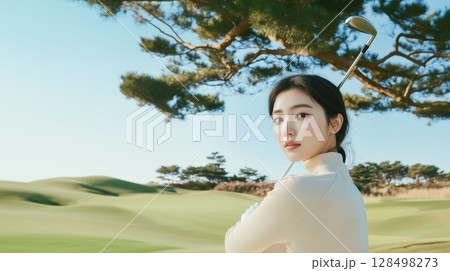 Beautiful Korean woman practices her swing on a golf course under a clear blue sky 128498273