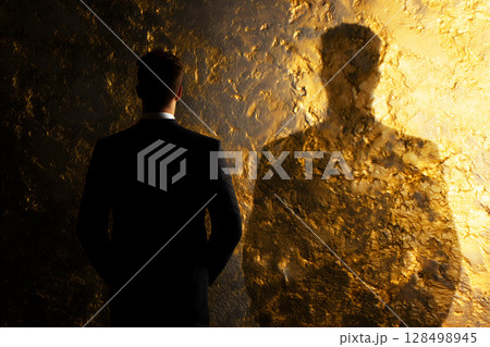 Businessman stands in front of golden wall, his shadow reflecting ambition and future possibilities 128498945