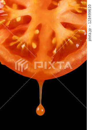 Natural tomato juice dripping from half a fresh tomato, black background 128499610