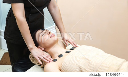 Woman with hot stones placed on her chest relaxes in a massage parlor Woman with hot stones placed on her chest relaxes in a massage parlor 128499644