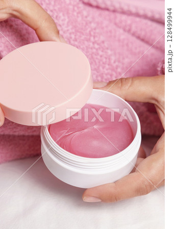 Woman in pink bathrobe holding eye patches jar with pink lid closeup, cosmetic mockup Woman in pink bathrobe holding eye patches jar with pink lid closeup, cosmetic mockup 128499944