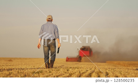 farmer working in wheat field, combine harvester ploughing in wheat field, agriculture tablet, seamless farm management, enhancing farm profitability, integration of technology in crop management 128500235
