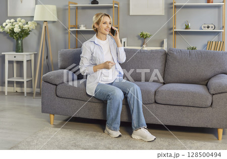 Happy young woman sitting on the sofa in the living room and talking on her mobile phone 128500494