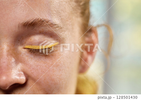 Dopamine makeup. Close-up of closed eye with bright yellow eyeliner in natural light 128501430