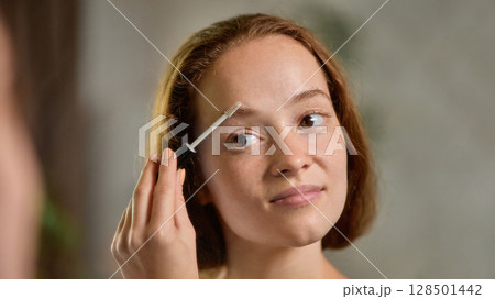 Clean-girl. Close-up portrait of calm woman brushing eyebrows with natural expression 128501442