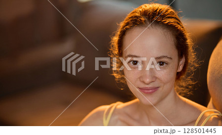 Smiling young woman with freckles looking at camera with warmth and calm expression Smiling young woman with freckles looking at camera with warmth and calm expression 128501445