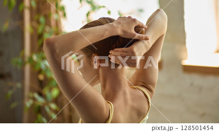 Clean-lazy hybrid. Rear view of woman calmly securing hair in cozy natural-lit interior Clean-lazy hybrid. Rear view of woman calmly securing hair in cozy natural-lit interior 128501454
