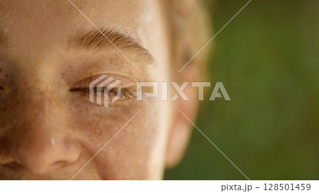 Extreme close-up of closed eye with freckles and peaceful emotion in soft daylight 128501459