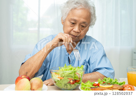 Asian elderly woman patient eating salmon steak breakfast with vegetable healthy food in hospital. 128502037