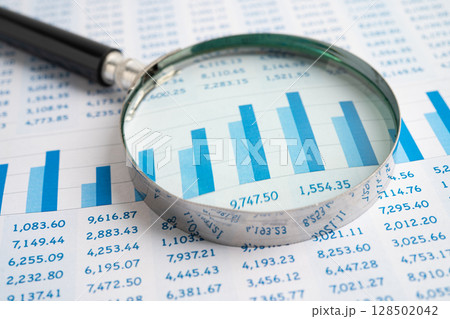 Magnifying glass on spreadsheet and graph paper. 128502042