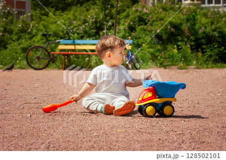 Toddler playing with a toy dump truck on a sunny playground day Toddler playing with a toy dump truck on a sunny playground day 128502101