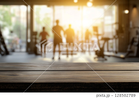 A close-up of a wooden table surface in the foreground, with a blurred gym interior and sunlit windows in the background. 128502789