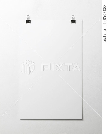 A blank white poster hangs on a grey wall, held by black binder clips. 128502888
